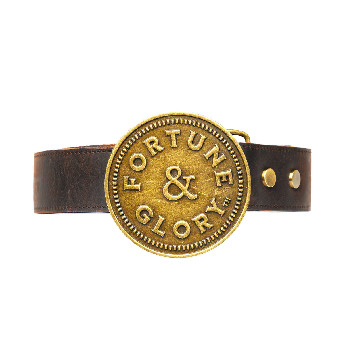 A brown leather belt featuring a large, round antique gold buckle engraved with the words 'FORTUNE & GLORY' and a central ampersand symbol.